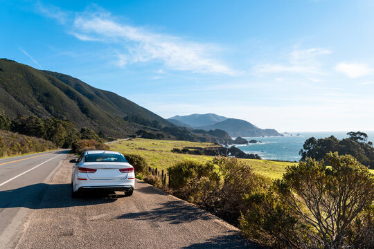 A White Car On Highway 1 In California. Beautiful Californian Coastline Of The Pacific Ocean At Big Sur During A Road Trip