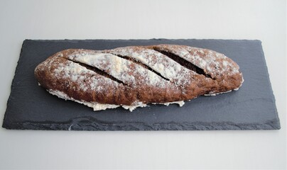 Homemade rye french mini baguette in flour, on a slate board. On a light background