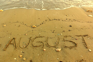 August Hand Written on Sandy Texture at a Sunny Beach with Pebbles with Sea Water in the Background. Travel in the Summer Months Tourism Wallpaper Image. Seascape Vacation Concept.