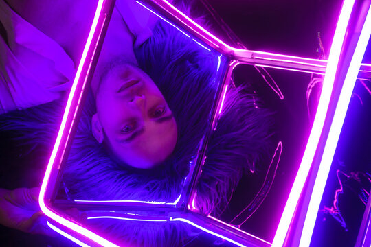 Portrait of the Young Handsome emotional man in an unbuttoned white shirt with neon coub. Neon Room. Old 90's retro style. Reflect of neon words near male. Selective focus.