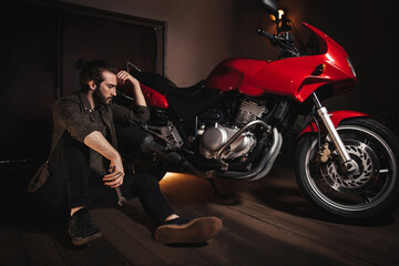 Fototapeta na wymiar A man holds a tool and thinks how to fix a motorcycle. A man sits on the floor in a garage