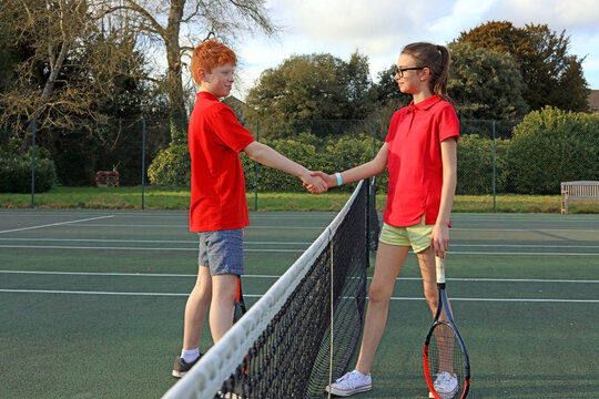 A teenage girl and boy sharing a sportsmanship hand shake at the end of a game of tennis