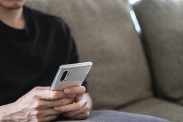 man is using a smartphone for the internet while relaxed sitting on the sofa at his modern home. young people are texting on mobile devices while on the couch. a guy is holding the telephone.