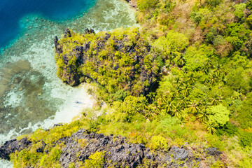 Aerial drone view of secluded beach in jungle with tropical coral reef and small sandy beach surrounded by huge cliffs