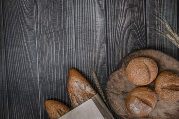 rustic crusty loaves of delicious fresh bakery bread and buns in a paper bag and on cutting board.on a wooden table. top view. flat lay.
