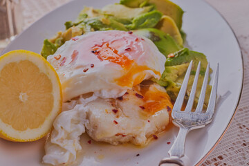 Healthy fish fillet of cod, with a poached egg on top,alongside some avocado.