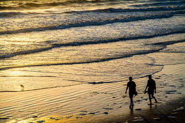 Fototapeta na wymiar Two men walking side by side on Santa Monica Beach in California USA during sunset