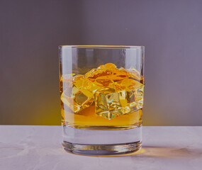 Whisky,bourbon,brandy with ice, shot on a marble surface, with a yellow grey gradient background.