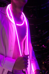 Portrait of the Young Handsome emotional man in an unbuttoned white shirt with flexible pink neon ribbon. Neon Room. Old 90's retro style. Reflect of neon words near male. Selective focus.