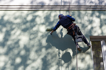 Industrial climber paints a building facade.
