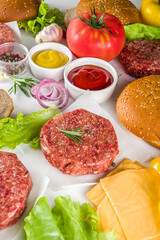 Cooking burger background. Set various cheeseburger  and beefburger ingredients - bun, tomatoes, onion, lettuce, sauces, cheese and raw burger cutlets, ready for barbecue grill. Burger bbq party fest 