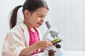 Indoor image of cute little girl working with microscope and exploring plants. The kid in lab coat learning science in the school laboratory. Child looking on the leaf through the microscope. - Powered by Adobe