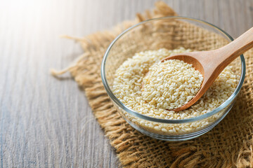 White sesame seeds in glass cup on wood table.