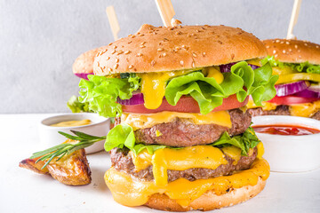 Tasty grilled homemade cheeseburgers with beef, tomato, cheese, tomato and lettuce. On grey background, with sauces. Top view copy space