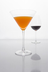photograph of a glass of orange cocktail in front and a glass of wine in the background with white background