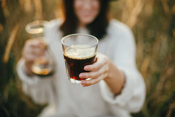 Hipster woman holding hot coffee in glass cup on background of rural herbs in sunset. Alternative coffee brewing outdoors in sunny light. Atmospheric rustic moment. Travel and Wanderlust