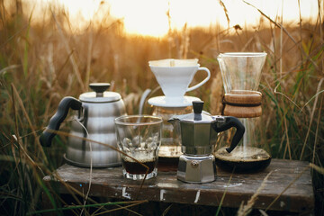 Alternative coffee brewing outdoors in travel. Steel kettle, hot coffee in cup, coffee dripper, ...