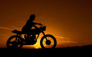 Fototapeta na wymiar Black silhouette of a girl on a retro custom bike. Motorcycle and girl on a background of sunset over the evening.