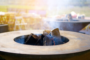 Round outdoor steel iron grill roaster with burning wood, heat smoke close-up photo of an open fire. The concept of a great outdoor recreation barbecue dishes on the grill of the best chef.
