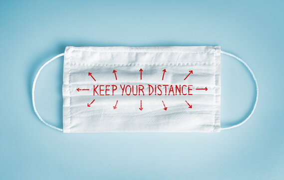 Covid-19 Coronavirus protection and social distancing concept: Medical disposable face mask with keep your distance message on blue background.  WHO recommends usage of mask for Coronavirus.