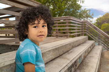 A young boy sits on the waterfront park steps to enjoy the view. The toddler looks at the camera...