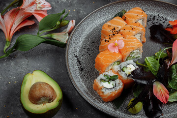 Delicious fresh sushi rolls with salmon and philadelphia cheese on gray plate on dark stone background. Traditional japanese seafood, healthy food concept