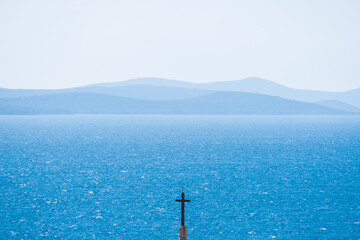 Minimalism photography of cross with turquoise sea and mountain in the background