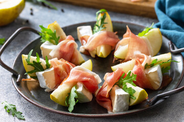 Summer snacks close-up. Pear appetizer with jamon, arugula and brie cheese on a light stone table.
