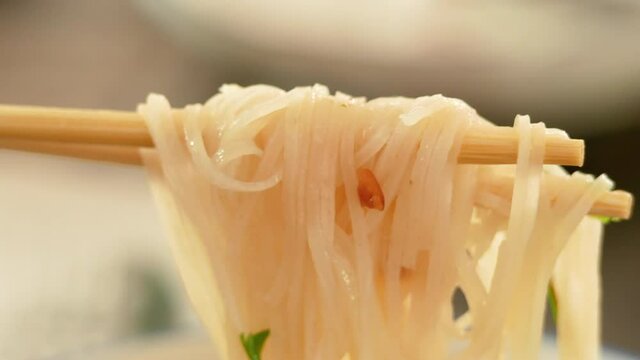 Close-up of hand use chopstick to pick noodles in a traditional Vietnamese beef soup Pho. Vietnamese style food.