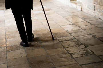 Old man legs walking with walking stick on stone tiles