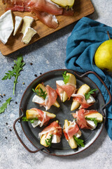 Summer snacks. Pear appetizer with jamon, arugula and brie cheese on a light stone table. Top view flat lay background.
