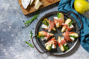 Summer snacks. Pear appetizer with jamon, arugula and brie cheese on a light stone table. Top view flat lay background. Copy space.