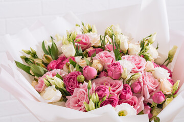 big bouquet of beautiful and bright white-pink roses and eustoma in pink packaging on a white wall background. close-up