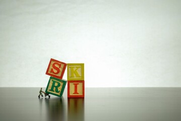 Isolated wooden letter block stacked to form RISK with miniature worker on job  Conceptual image of risk and uncertainty. 