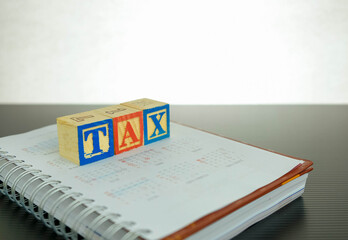 Conceptual image of annual tax return.  Wooden block letter forming TAX on note book over dark reflective surface. Focus at block letter A.