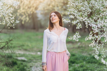 Amazing young woman posing in Blooming tree orchard at spring. Beautiful happy young woman enjoying smell in a flowering spring garden