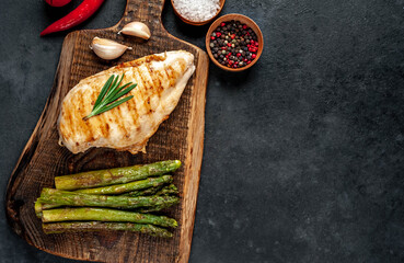 Grilled chicken breast with asparagus and spices on a cutting board on a stone background with copy space for your text.