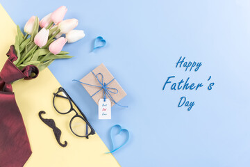 Happy Fathers Day background concept.Decorated red necktie, tulip, blue heart, mustache, eyeglasses, gift box with greeting card on bright pastel background with copy space. Top view, flat lay.
