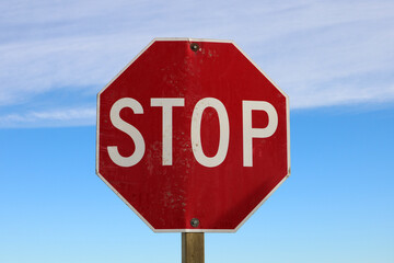 Bright red stop sign. Red sign against a blue sky with a band of high altitude clouds. An visual...