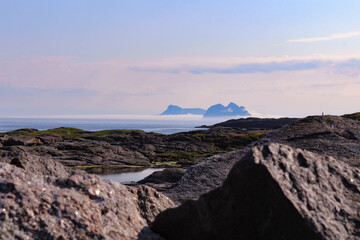 Fototapeta na wymiar Mystérieuse île entourée de brume avec rochers au premier plan dans les Lofoten en Norvège