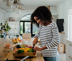 Young woman chopping vegetables in kitchen at home, happy and smiling - Powered by Adobe