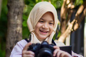 Muslim School kid.Pretty little girl in hijab using camera with happy face.Concept of modern Muslim...