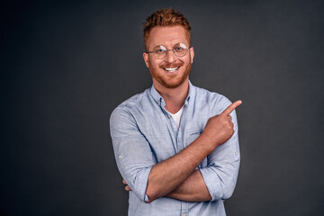 Indoor shot of good-looking confident and bossy male entrepreneur in shirt and glasses with red hair, pointing at upper right corner and smirking, knowing what is good for business, giving good advice