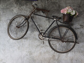 Fototapeta na wymiar The old black bicycle with a flower basket at the end is hung on a concrete wall to decorate the place to look beautiful.