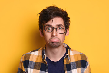 Portrait funny young man in glasses and casual clothes looking at camera isolated over yellow...