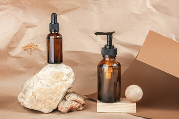 Naklejka premium Brown glass bottles of cosmetic products on stone and wooden geometric shapes on beige craft paper background. Natural Organic Spa Cosmetic Beauty concept Front view Mockup