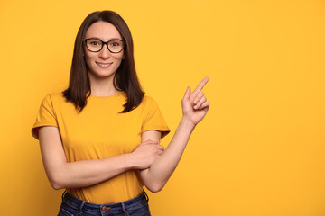 Beautiful smiling girl in eyeglasses pointing  with index finger at copy space for advertisement,...