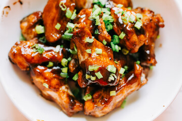 A close-up of sticky chicken wings glazed with a sweet sauce made with honey and soy sauce. This plate of grilled wings is topped with green onions. Asian cuisine and Chinese cooking. 