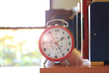 Naklejka premium Close-up of the red alarm clock on the library bookshelf selective focus and shallow depth of field