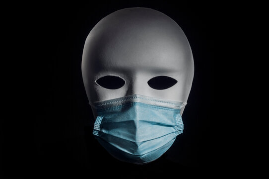 White theatrical mask wearing a surgical mask on black background